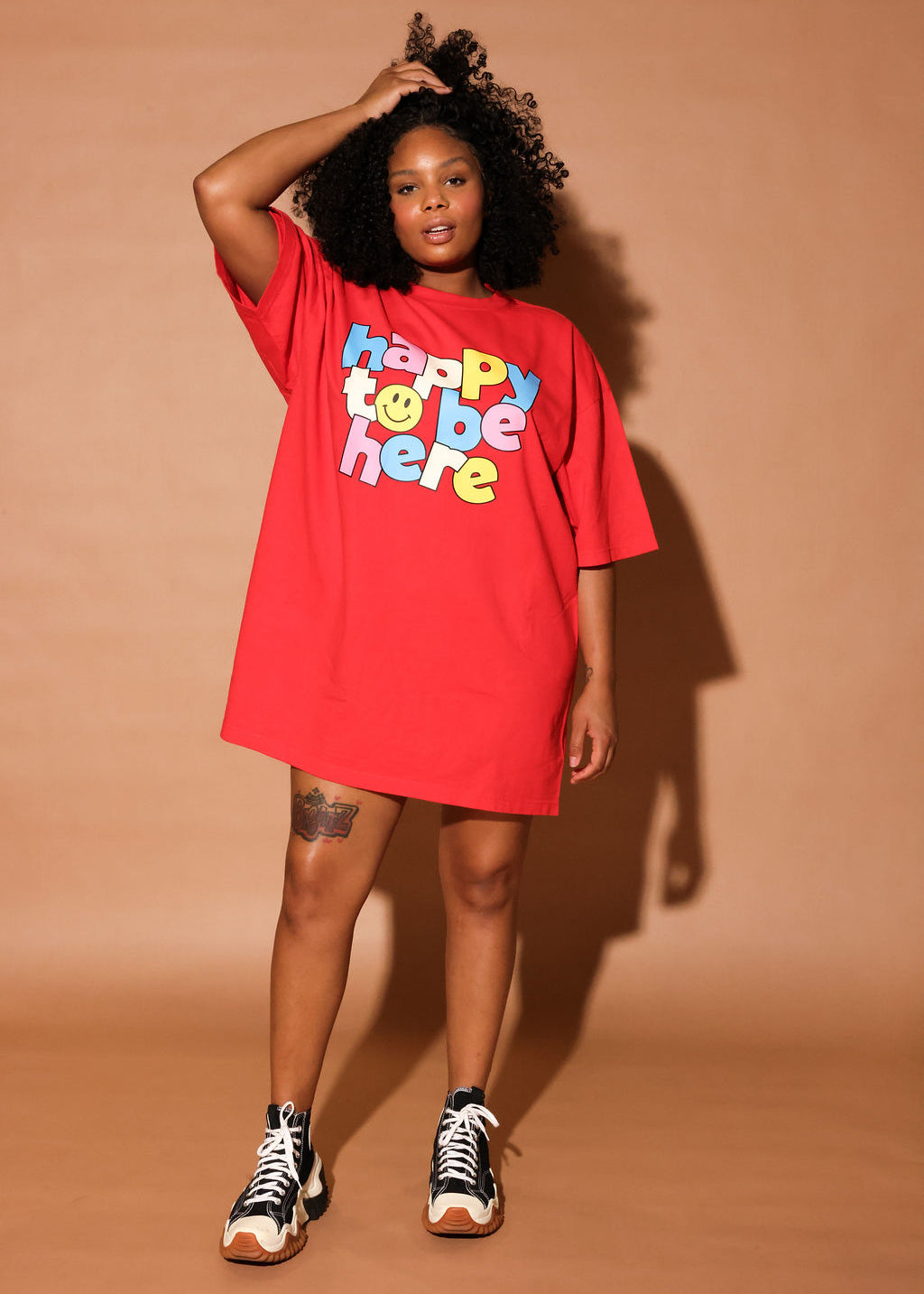 Model wearing a red t-shirt with colorful 'happy to be here' text on a white background, frontal view