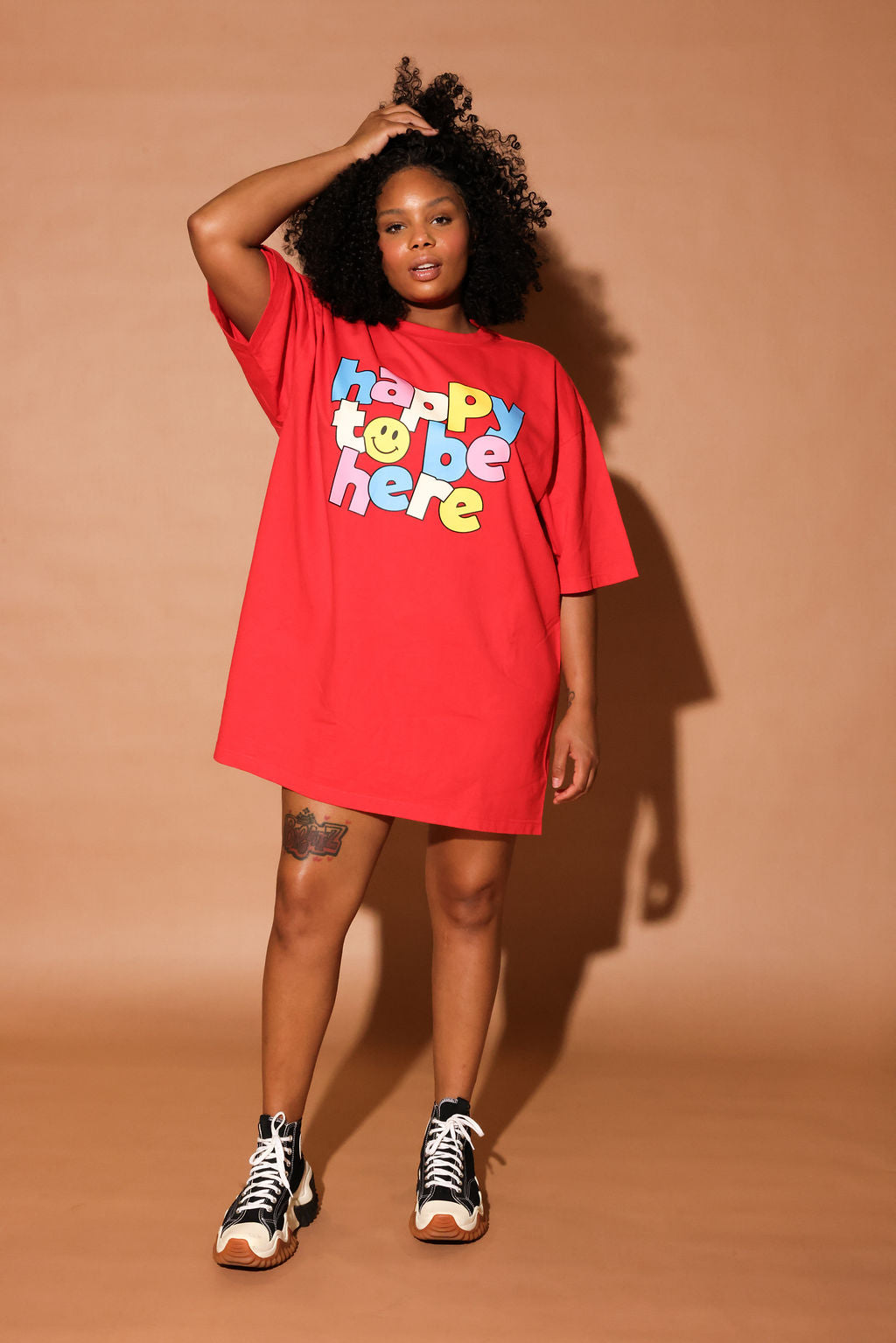 Model wearing a red t-shirt with colorful 'happy to be here' text on a white background, frontal view