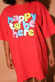 Model wearing a red t-shirt with colorful 'happy to be here' text on a white background, close up frontal view