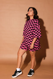 Woman wearing a pink and black checkered biker set against a brown background, frontal view