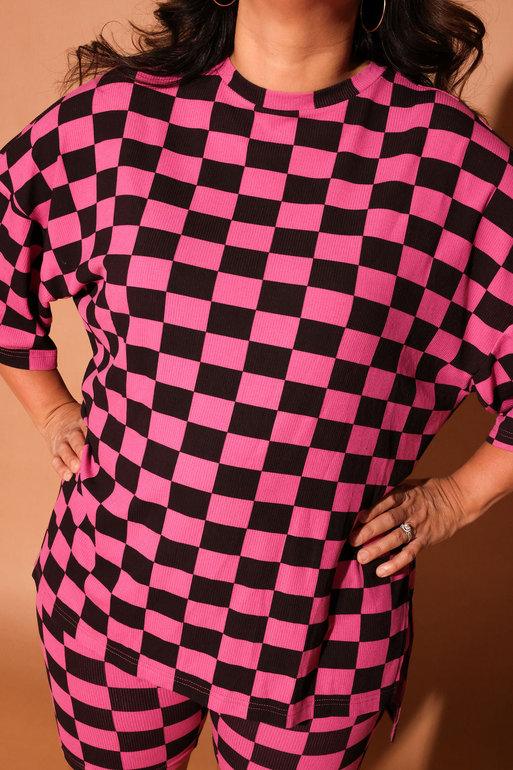 Woman wearing a pink and black checkered biker set against a brown background, close up frontal view