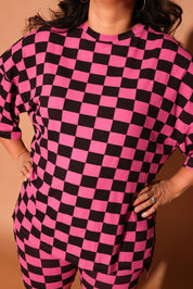 Woman wearing a pink and black checkered biker set against a brown background, close up frontal view