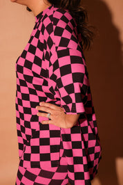 Woman wearing a pink and black checkered biker set against a brown background, side view