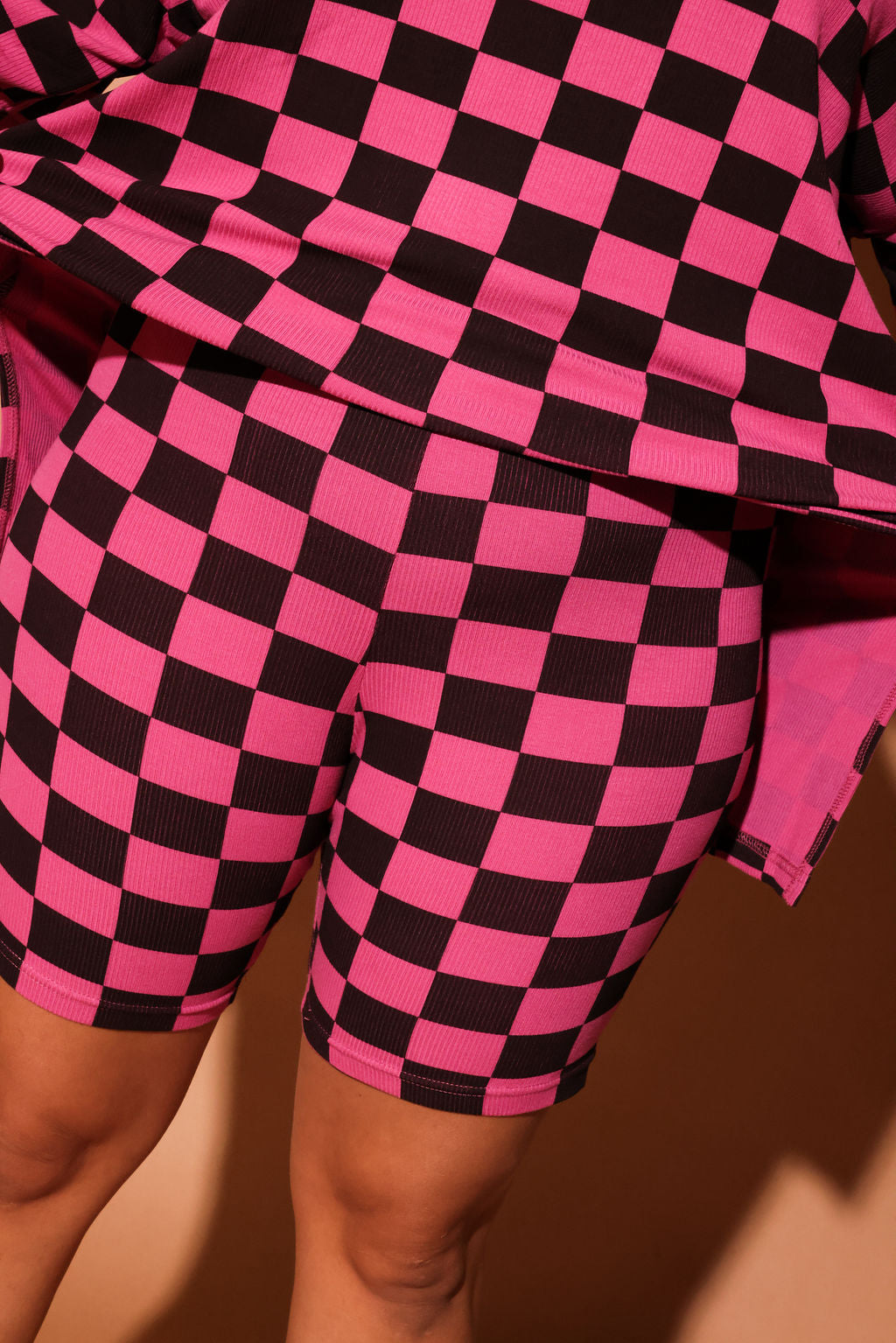 Woman wearing a pink and black checkered biker set against a brown background, close up frontal view
