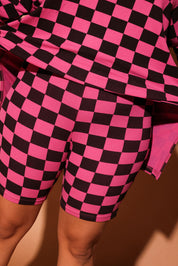Woman wearing a pink and black checkered biker set against a brown background, close up frontal view