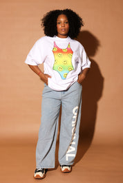 Model wearing a white t-shirt with a colorful swimsuit graphic and light blue jeans on a beige background, frontal view