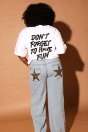 Model wearing a white t-shirt with text and light blue jeans with star designs on a brown background, back view