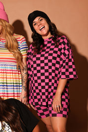 Woman wearing a pink and black checkered dress standing against a brown background