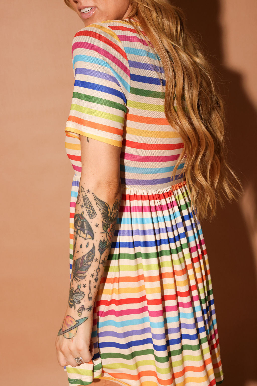 Person wearing a colorful striped dress with a tattooed arm on a brown background, side view