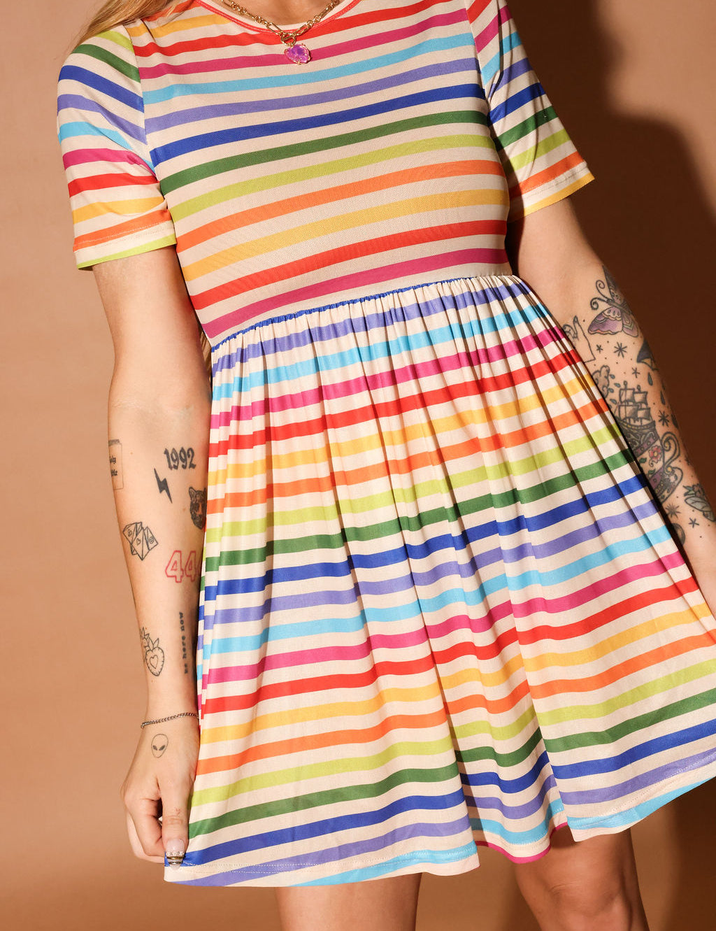 Woman wearing a colorful striped short dress and pink beanie against a brown background, close up frontal view