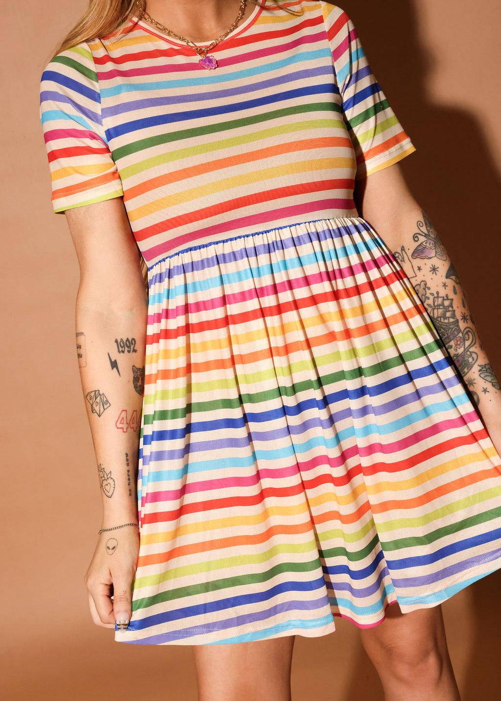 Woman wearing a colorful striped short dress and pink beanie against a brown background, close up frontal view