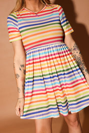 Woman wearing a colorful striped short dress and pink beanie against a brown background, close up frontal view