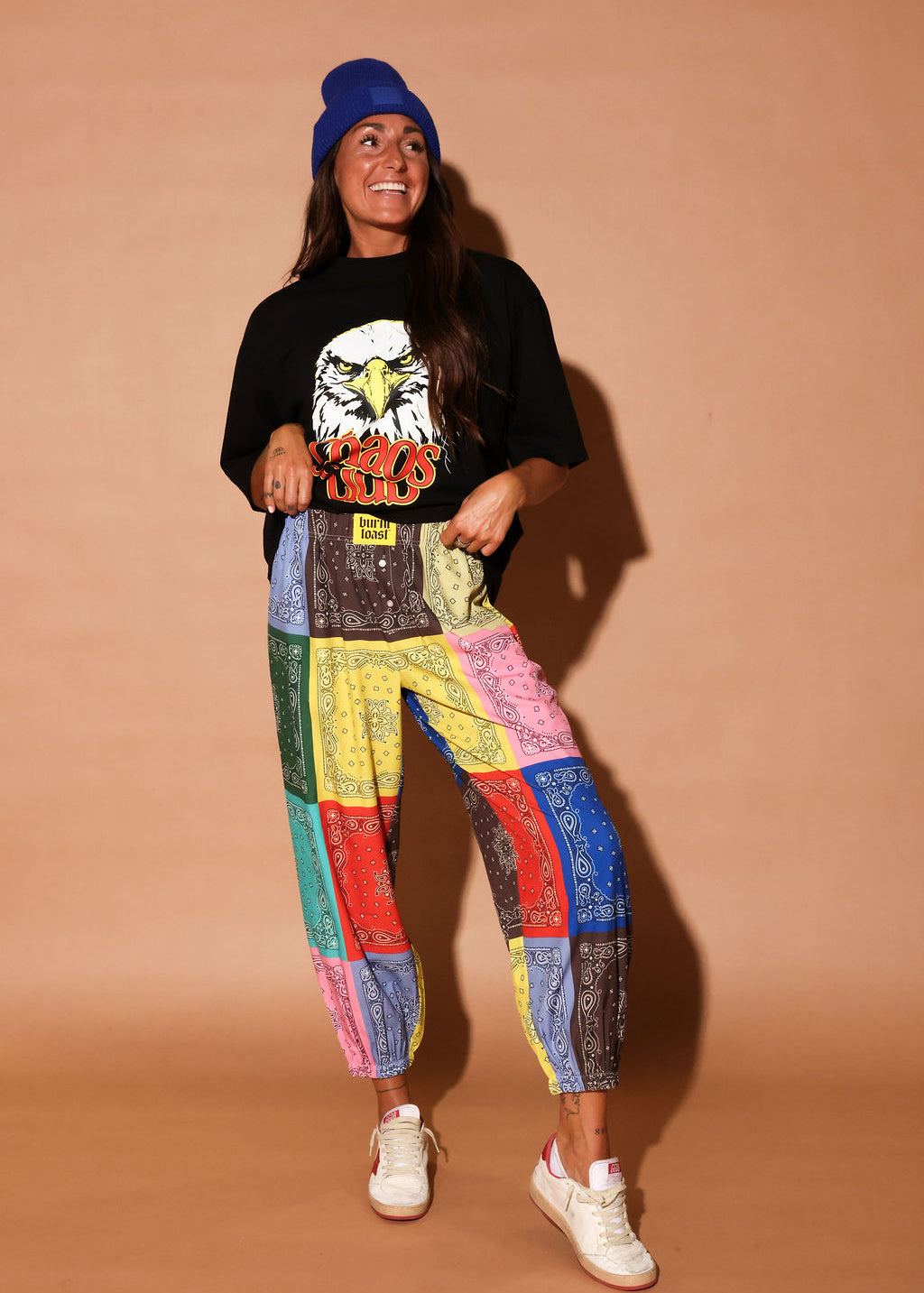 Person wearing a black t-shirt with an eagle graphic and colorful bandana pants on a beige background, frontal view