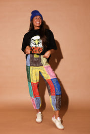 Person wearing a black t-shirt with an eagle graphic and colorful bandana pants on a beige background, frontal view