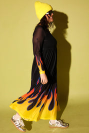 A model wearing a black mesh dress with flames at the bottom and a yellow beanie on a pale yellow background