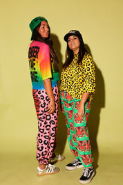 Two models wearing colorful outfits, the pants are loose fitting and the tops are cropped short sleeve, and trucker hats against a pale yellow background
