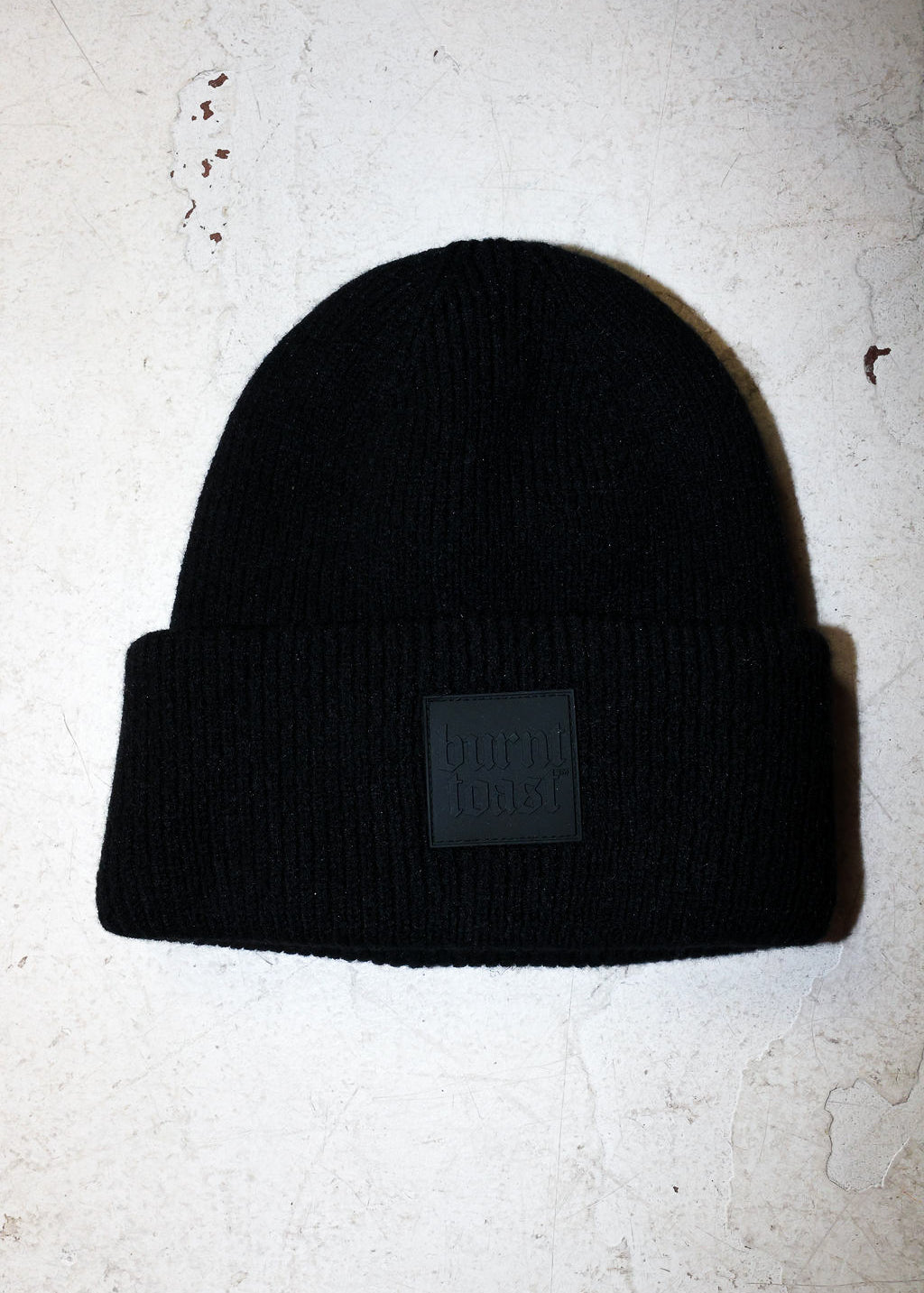 A black beanie with a burnt toast label on a white textured background