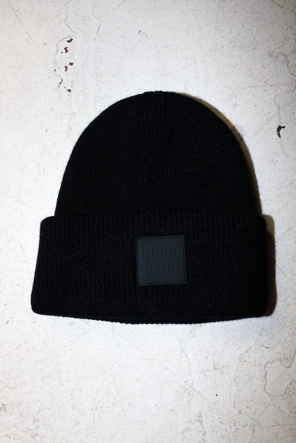 A black beanie with a burnt toast label on a white textured background