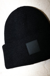 Close up of a black beanie with a burnt toast label on a white textured background