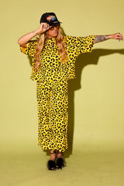 Model wearing a black and yellow leopard set black high heels and a black trucker hat that says 'mother' on it, against a pale yellow background