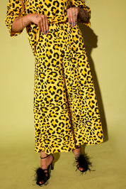Model wearing a black and yellow leopard set black high heels holding the waistband, against a pale yellow background