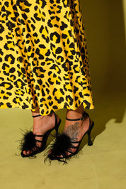 Model wearing a black and yellow leopard set black high heels, against a pale yellow background