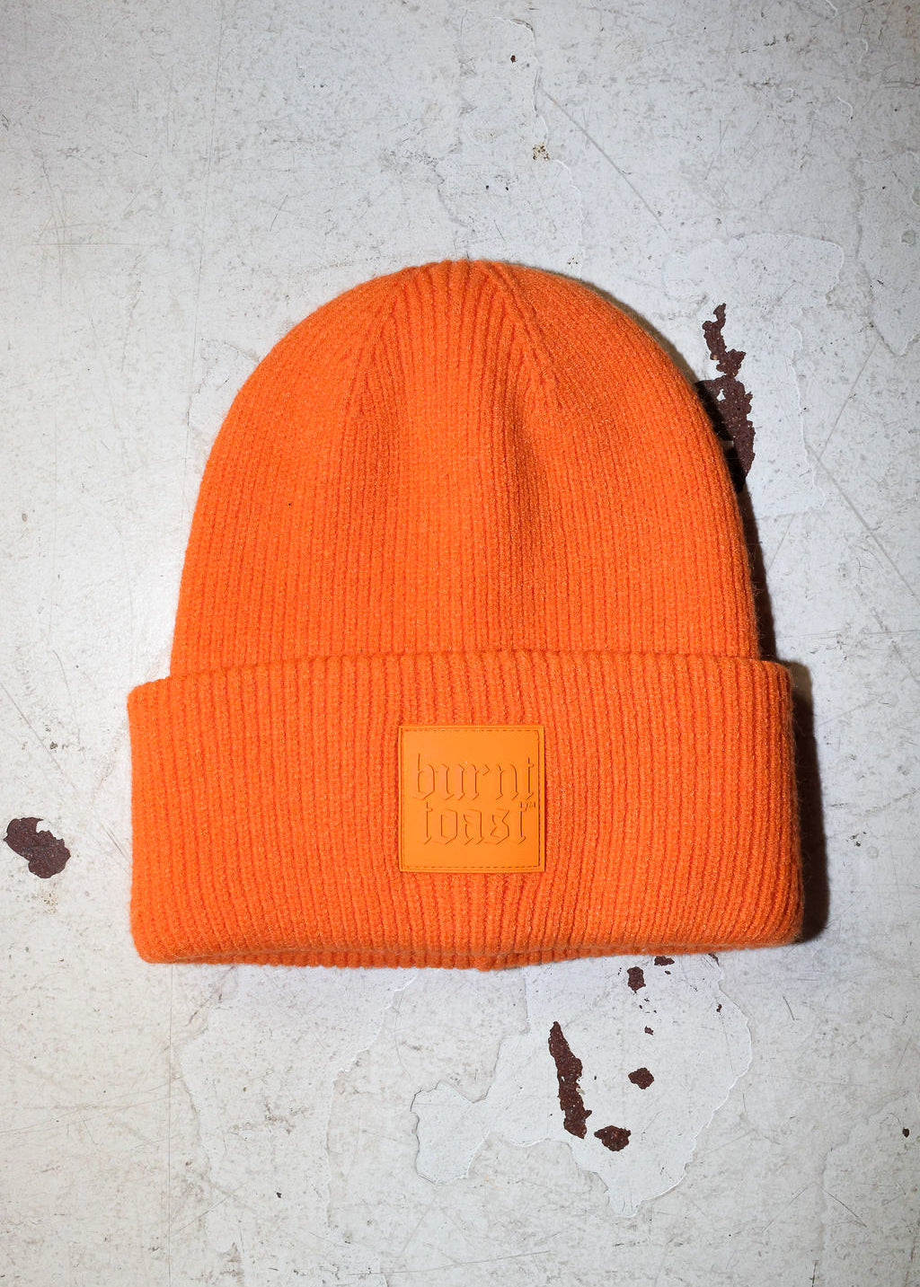 An orange beanie with a burnt toast label on a white textured background