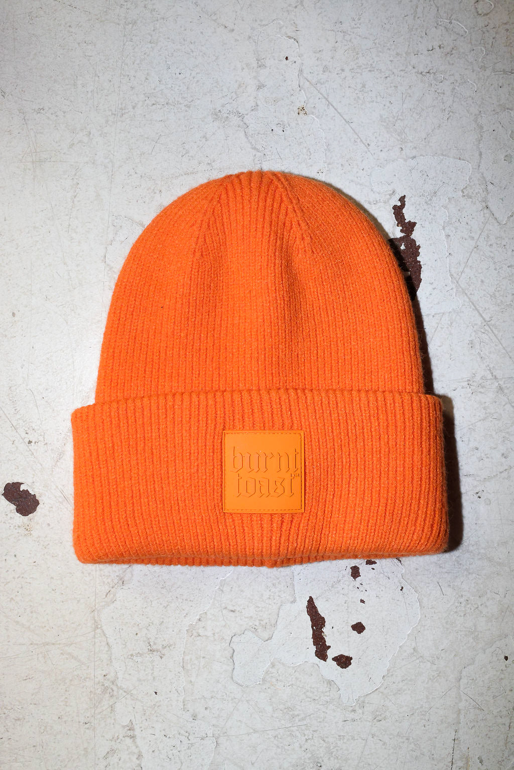 An orange beanie with a burnt toast label on a white textured background