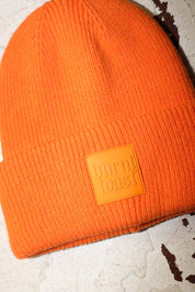 Close up of an orange beanie with a burnt toast label on a white textured background