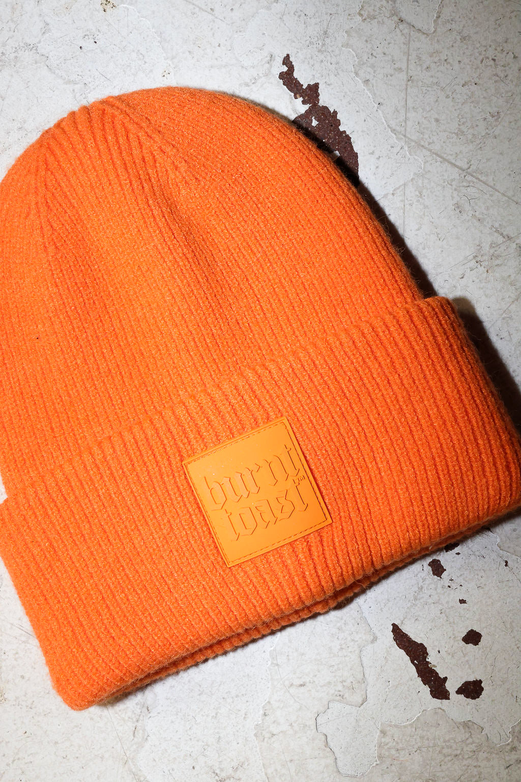 Close up of an orange beanie with a burnt toast label on a white textured background