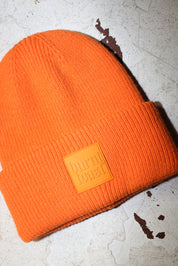 Close up of an orange beanie with a burnt toast label on a white textured background