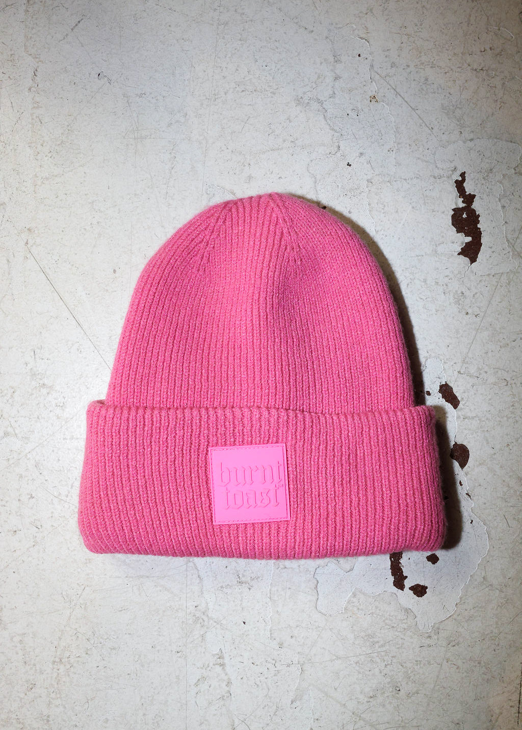 A pink beanie with a burnt toast label on a white textured background