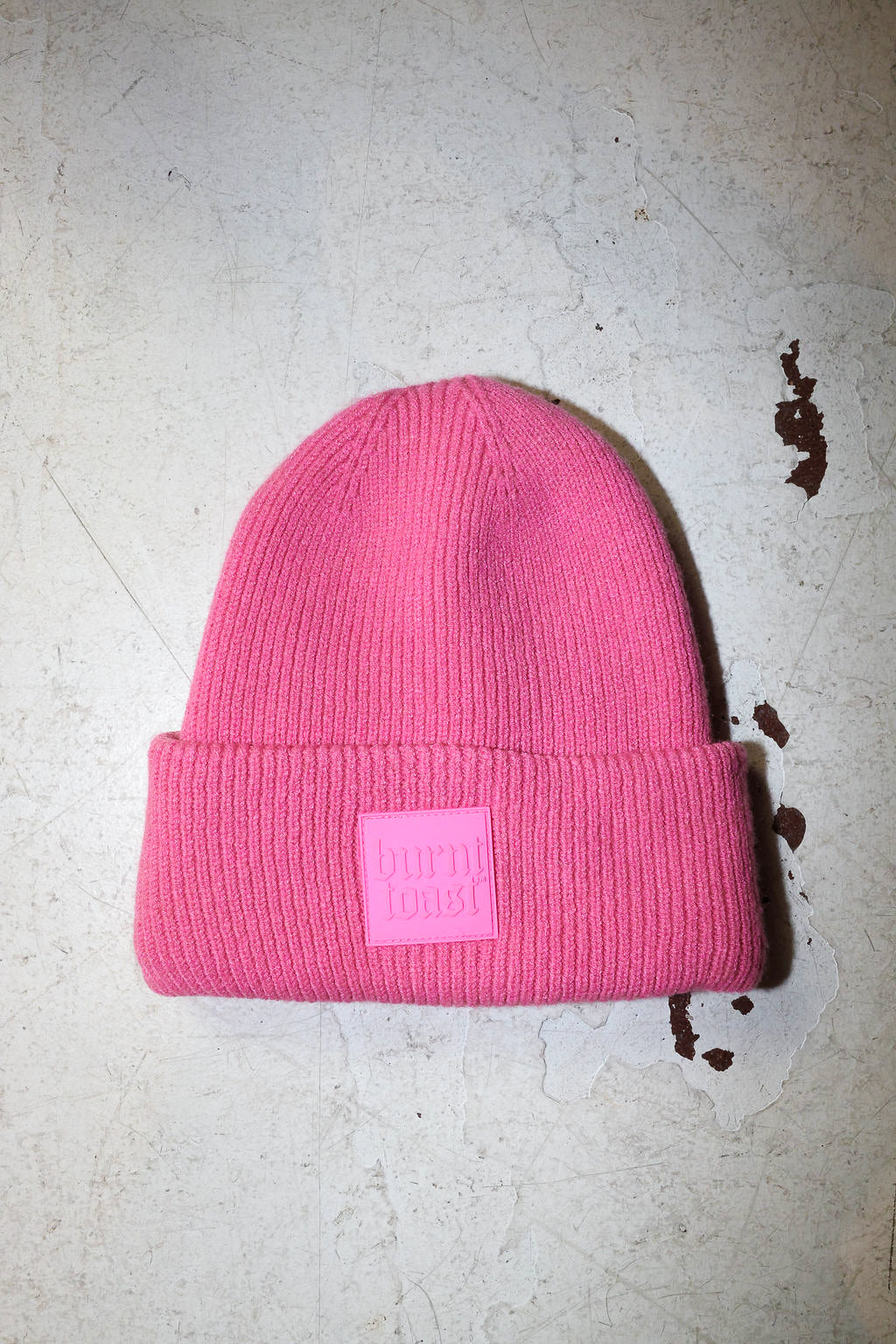 A pink beanie with a burnt toast label on a white textured background