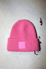 A pink beanie with a burnt toast label on a white textured background