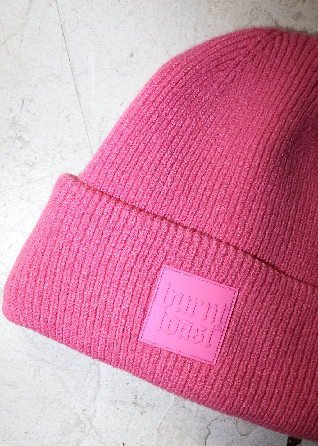 Close up of a pink beanie with a burnt toast label on a white textured background
