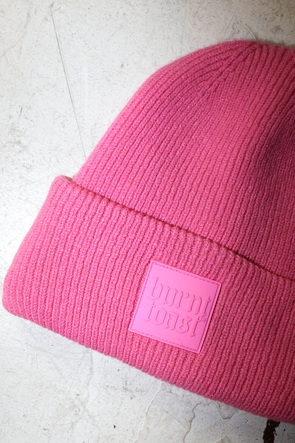 Close up of a pink beanie with a burnt toast label on a white textured background