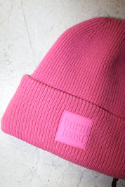 Close up of a pink beanie with a burnt toast label on a white textured background