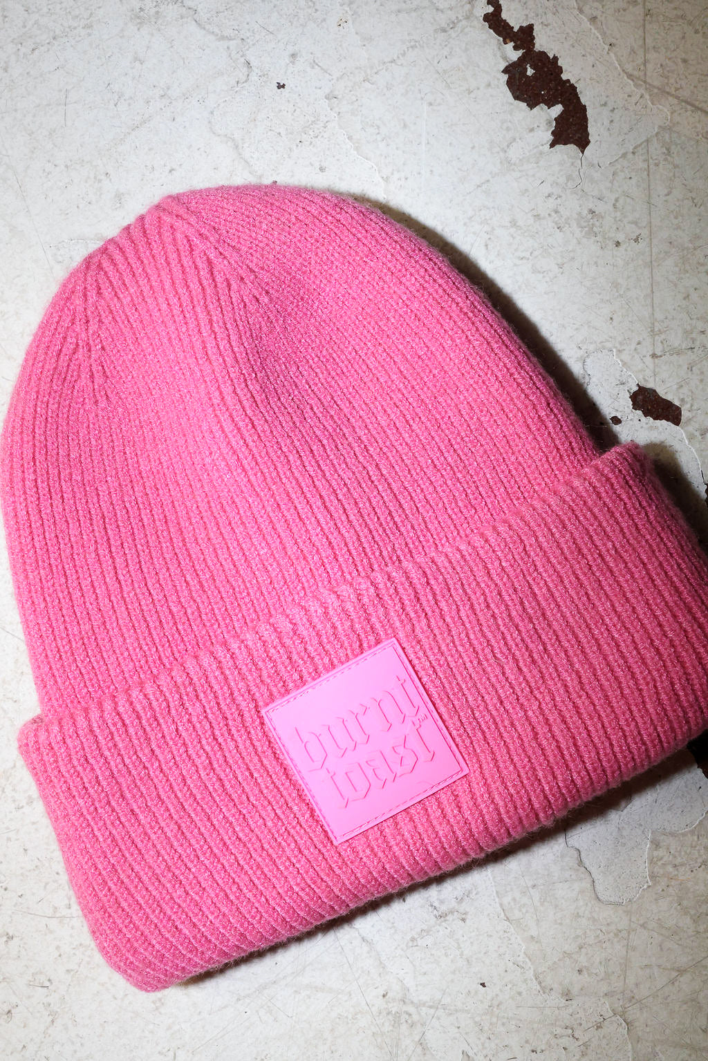 A pink beanie with a burnt toast label on a white textured background