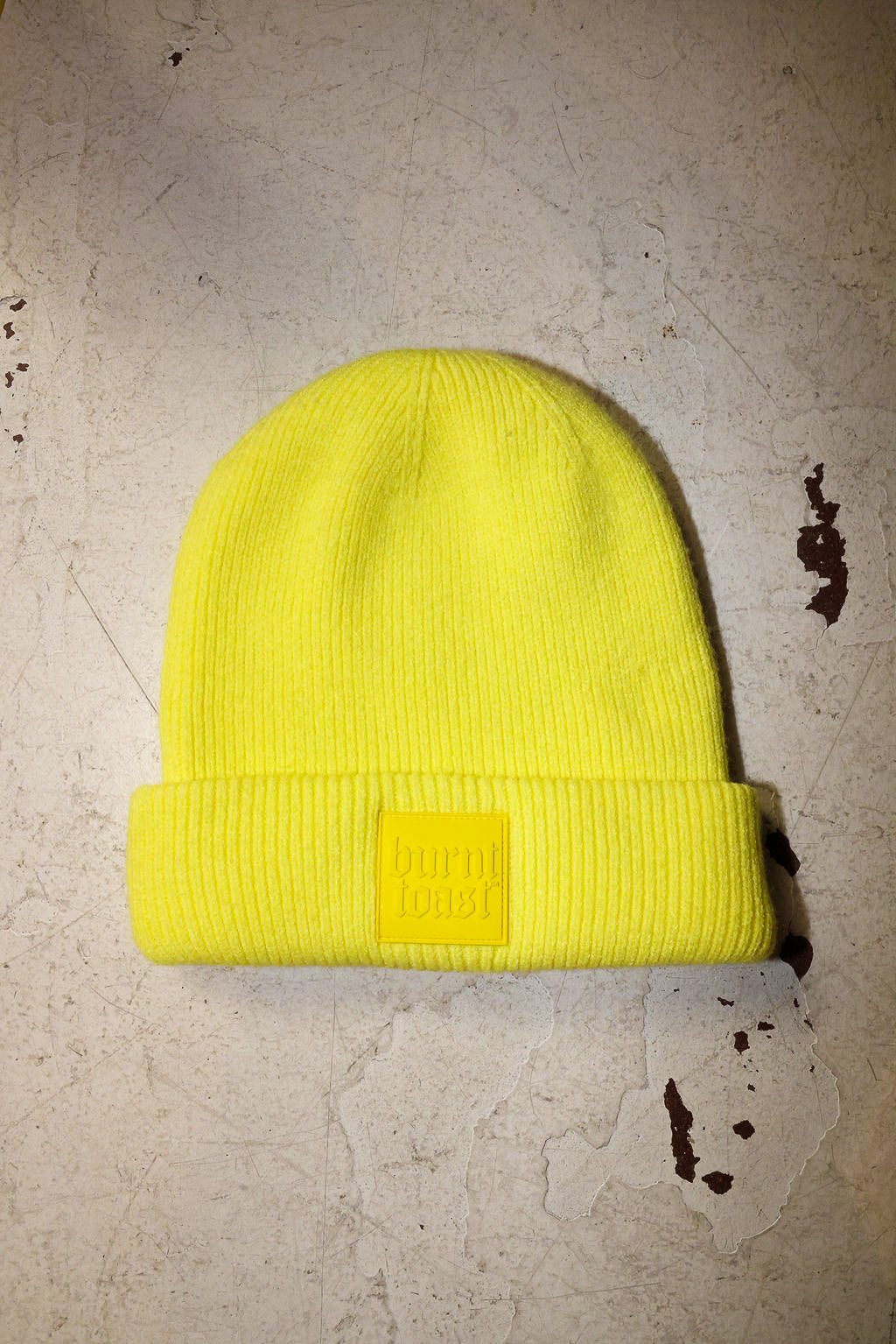 Yellow beanie with a Burnt Toast tag on a white textured surface
