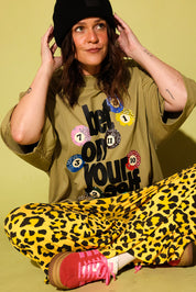 Model wearing a black and yellow leopard set a green graphic tee, and a black beanie, sitting against a pale yellow background