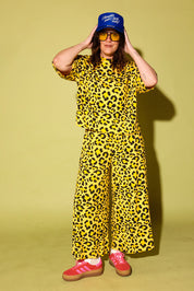 Model wearing a black and yellow leopard set black high heels and a blue trucker hat with text on it, standing against a pale yellow background