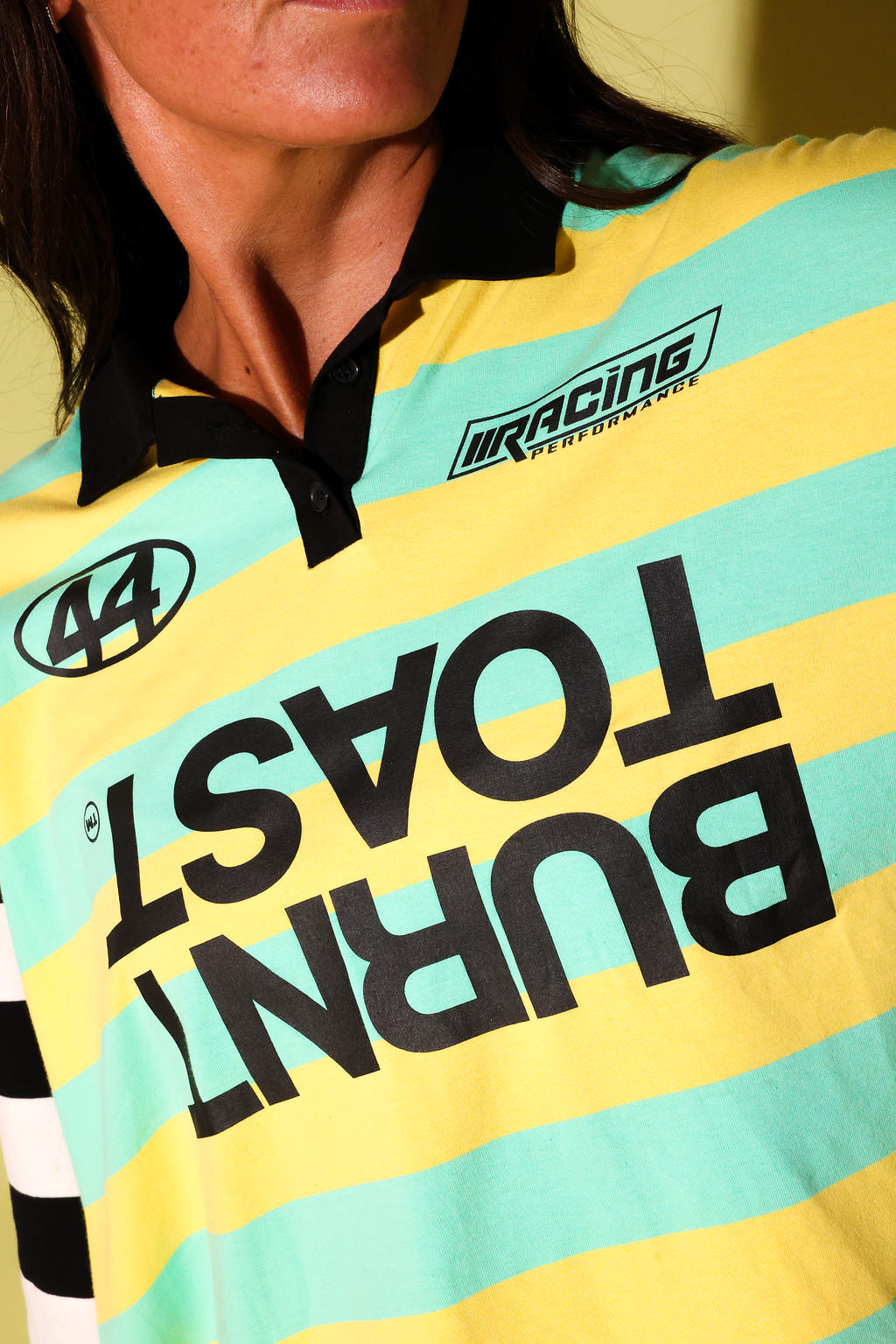 Close-up of a person wearing a striped racing-style polo shirt with black collar and large black text reading 'BURNT TOAST' across the front, plus a visible 'IRACING' logo.