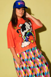 Model wearing a blue trucker hat with the text 'have fun, okay?' in pink and a orange graphic mesh top and diamond pattern plisse skirt on a pale yellow background