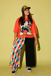 Model wearing an orange mesh top with a cow and rainbow graphic and colorful pants on a yellow background