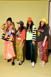 A group of four models wearing different colorful outfits with combinations of a skirt and cardigan, and pants and graphic tops against a pale yellow background