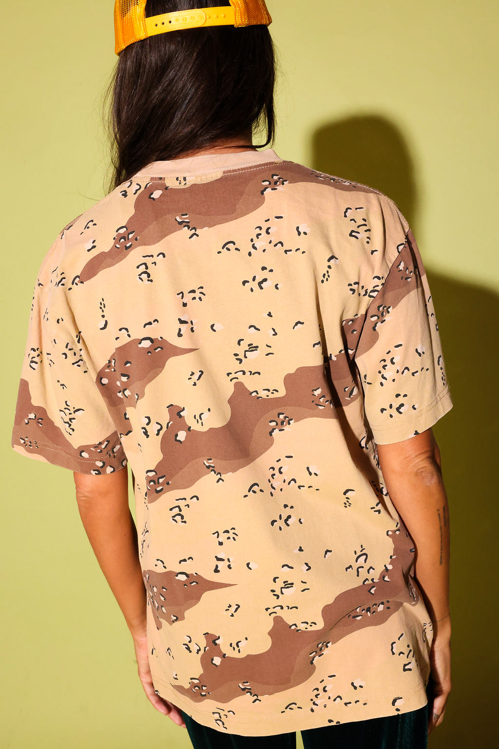 Back view of a model wearing a camo shirt on a pale yellow background