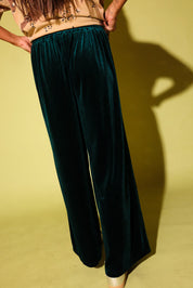 Back view of a  model wearing green velvet pants, on a pale yellow background
