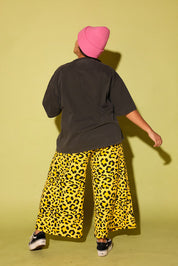 Back of a model wearing a grey shirt with black and yellow pants and a pink beanie on a pale yellow background
