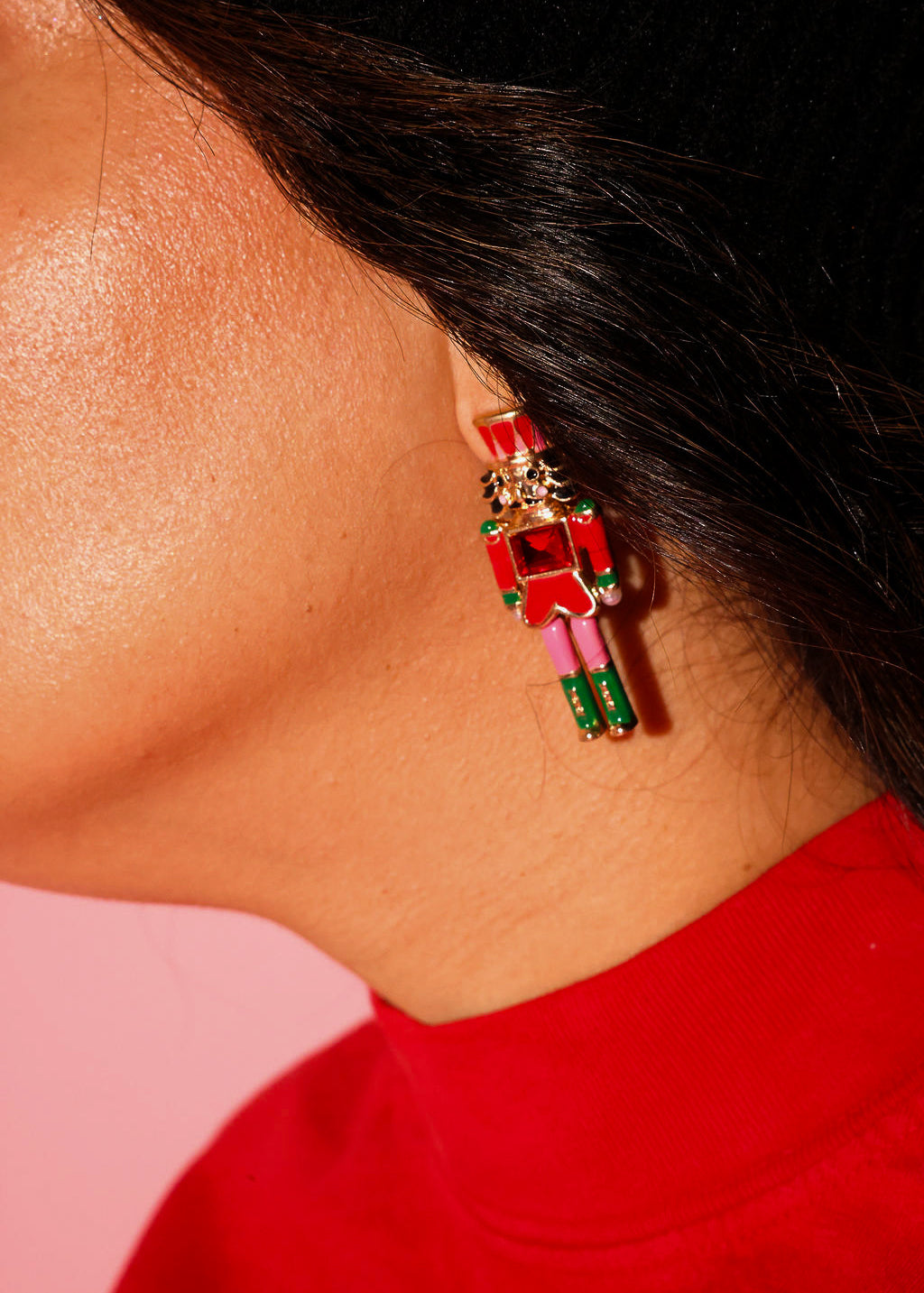 Close up of a model wearing a red crewneck with earrings in the shape of a nutcracker