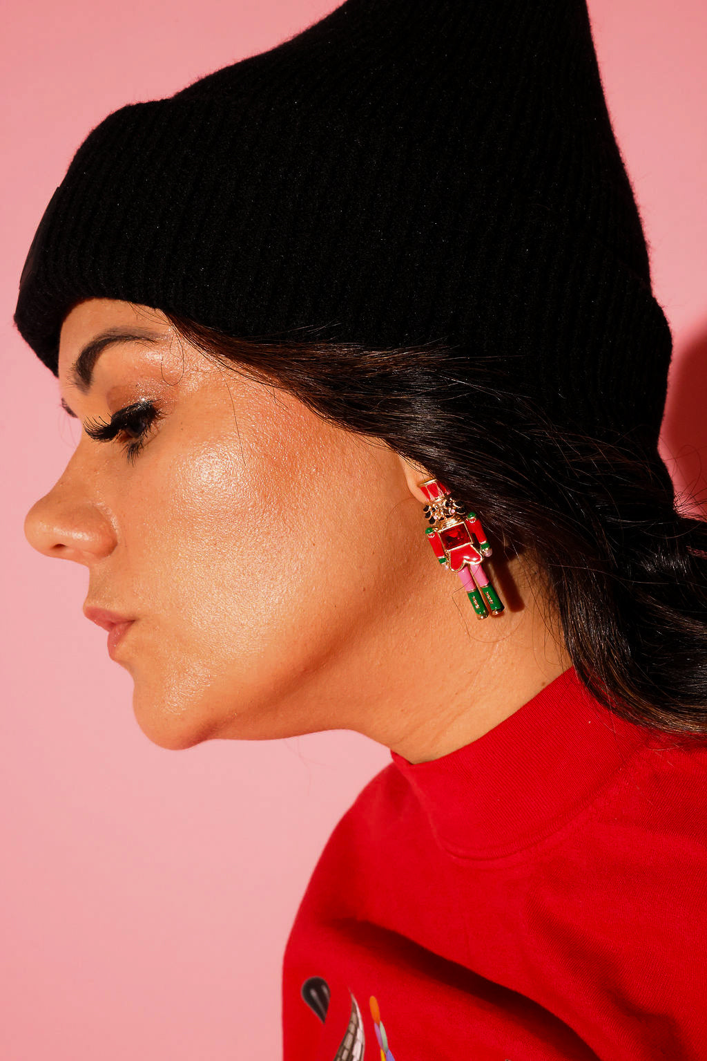 A model wearing a red crewneck and black beanie with earrings in the shape of a nutcracker